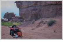 An ATV parked on a sandy trail beside impressive rock formations, highlighting the rugged outdoor landscape ideal for adventurous activities.